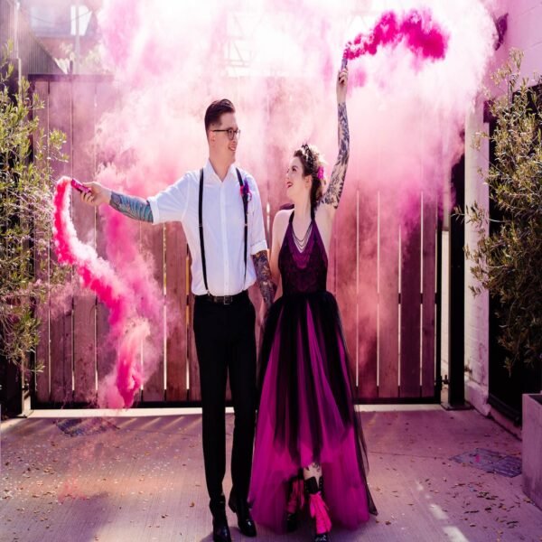 Fumigène à main rose en pleine activation, diffusant une fumée dense et colorée dans un espace extérieur.